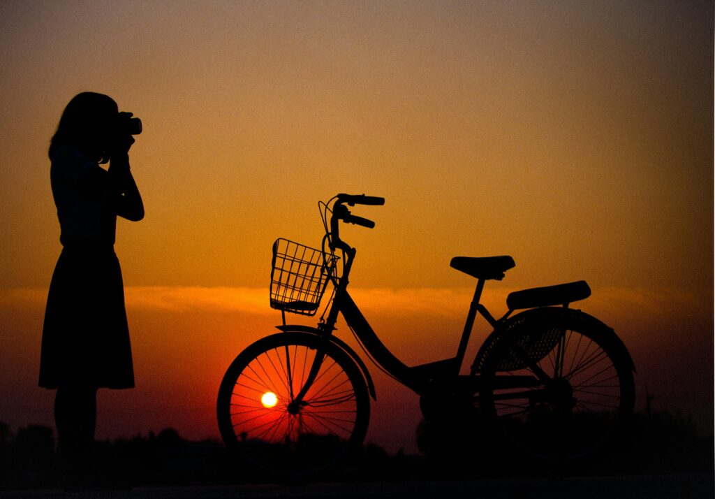 A woman, standing in front of her bicycle, taking a picture of the setting sun